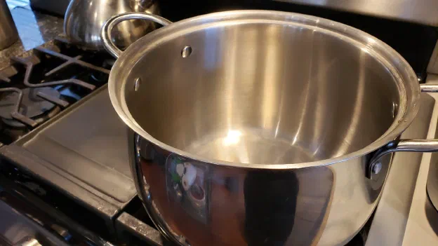 An empty stainless steel pot on a gas stove, ready for the jam