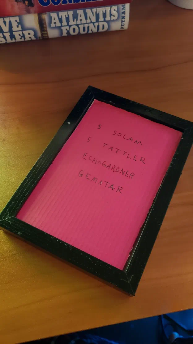 A charm card in a black frame, the words lettered on bright pink paper