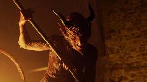A horned figure with a staff in torchlight