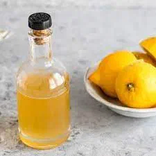 A corked bottle of golden hibiscus-lemon syrup beside a dish of lemons