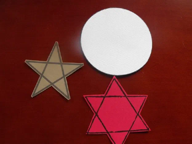Cut paper shapes on a table: a gold five-pointed star, a plain white disc, and a red six-pointed star