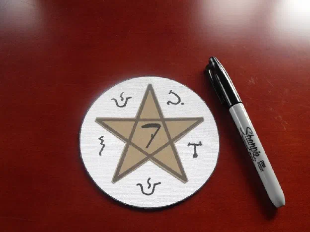 A white disc bearing a gold pentagram lettered with planetary sigils, a marker beside it