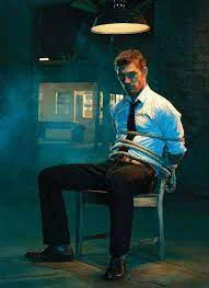 A man bound to a chair in a dim room