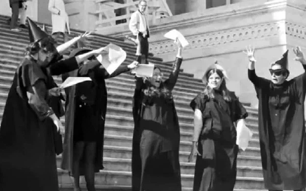 People in witch costume gathered on courthouse steps, holding papers aloft